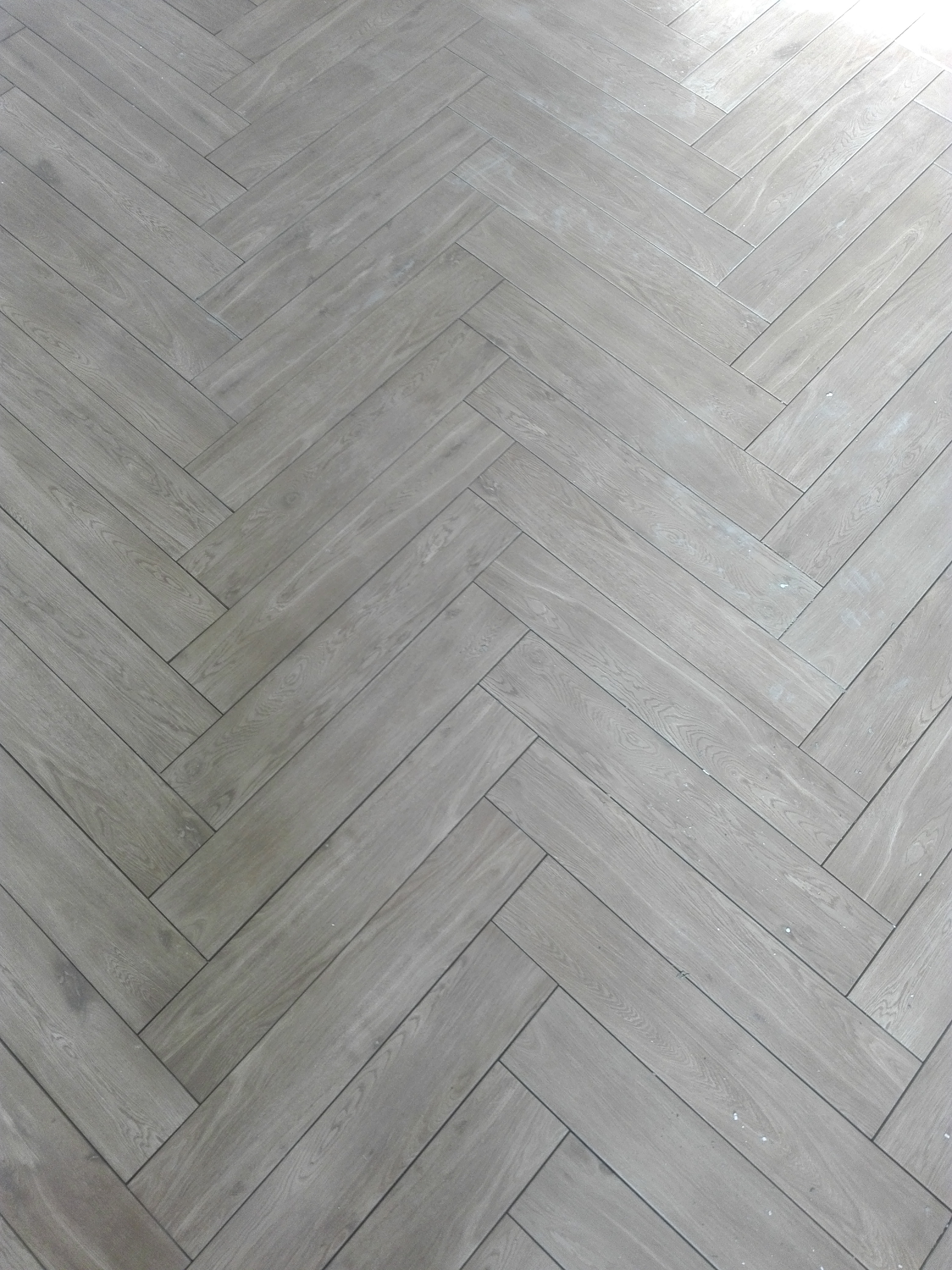 Jasnoszara podłoga ułożona w jodełkę, widoczne drobne zabrudzenia po montażu.