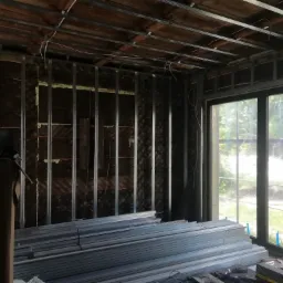 Konstrukcja z profili metalowych na ścianie i suficie, przygotowana pod montaż płyt kartonowo-gipsowych; widoczne ocieplenie ścian pianką montażową, stos metalowych profili na podłodze oraz okno...