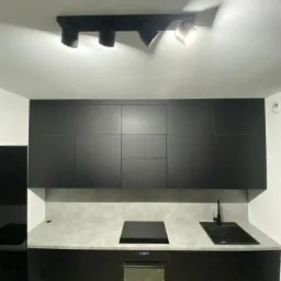 Czarna, minimalistyczna zabudowa kuchenna w mieszkaniu w Gliwicach, z matowymi frontami szafek, blatem imitującym beton, czarną armaturą i oświetleniem punktowym.