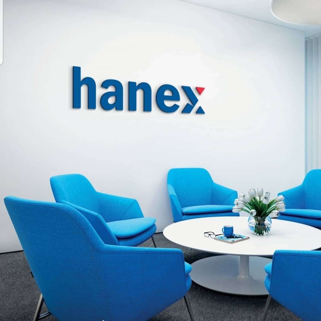Jasne wnętrze biura z niebieskimi fotelami ustawionymi wokół okrągłego białego stołu, na ścianie logo firmy Hanex