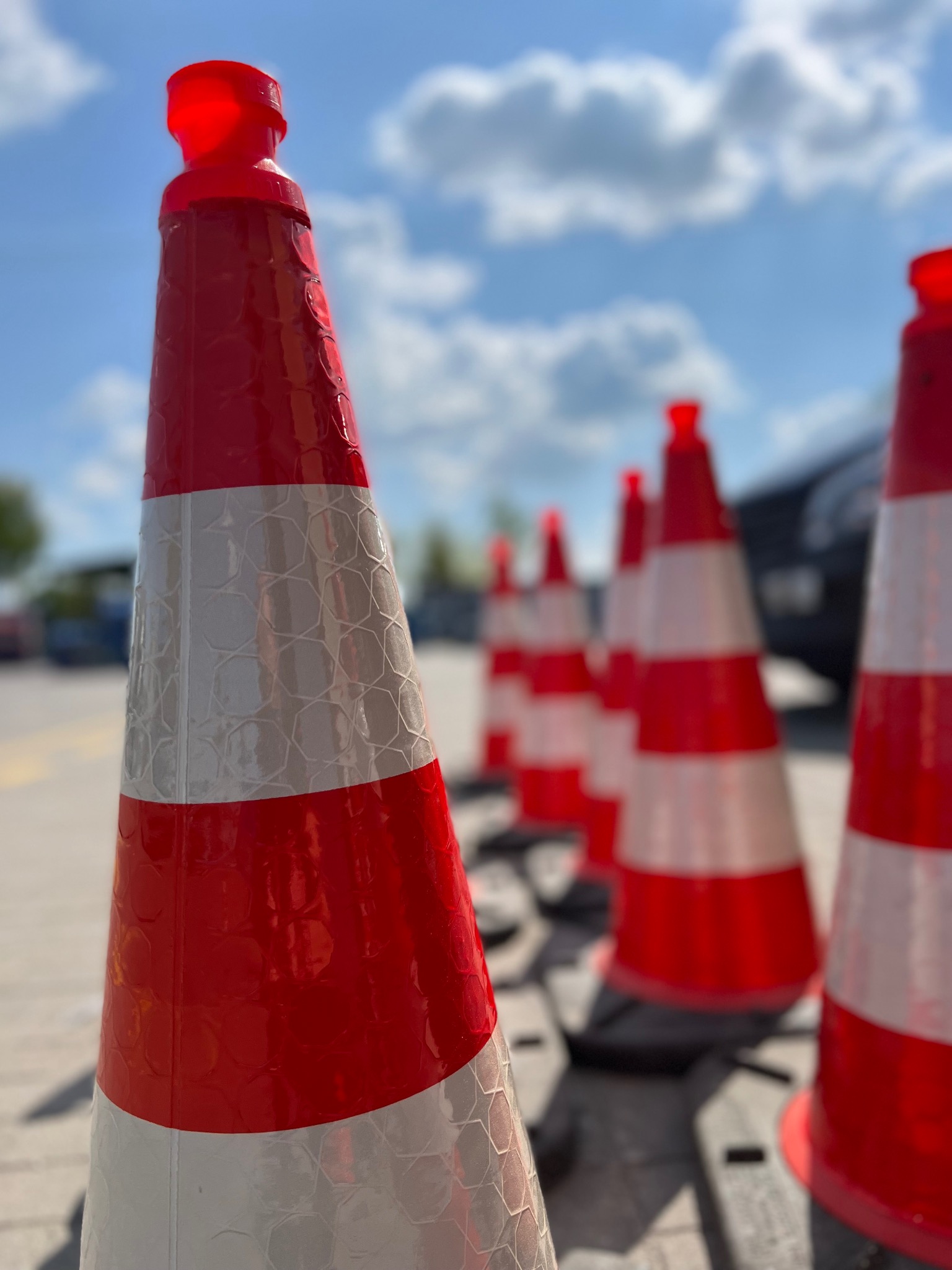 Rząd czerwono-białych pachołków drogowych z odblaskowymi pasami, ustawionych na betonowej nawierzchni w Ludomy, z błękitnym niebem w tle.