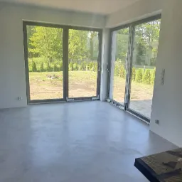 Jasne wnętrze z podłogą z mikrocementu, widok na ogród przez duże okna przesuwne.