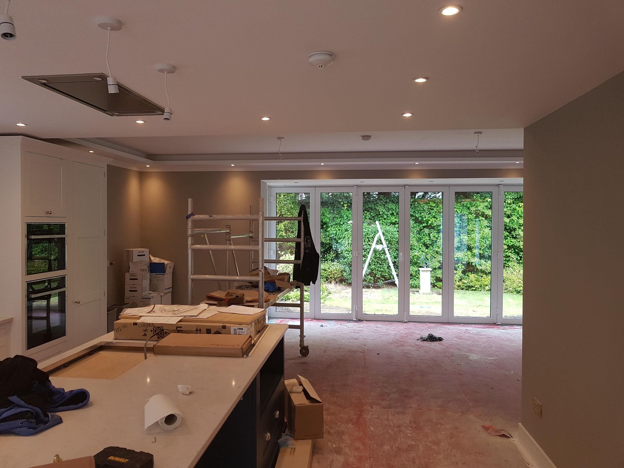 Wnętrze w trakcie remontu w Gdańsku: widoczna kuchnia z wyspą, rozłożone kartony, drabina malarska i duże okno balkonowe, sugerujące etap prac wykończeniowych.