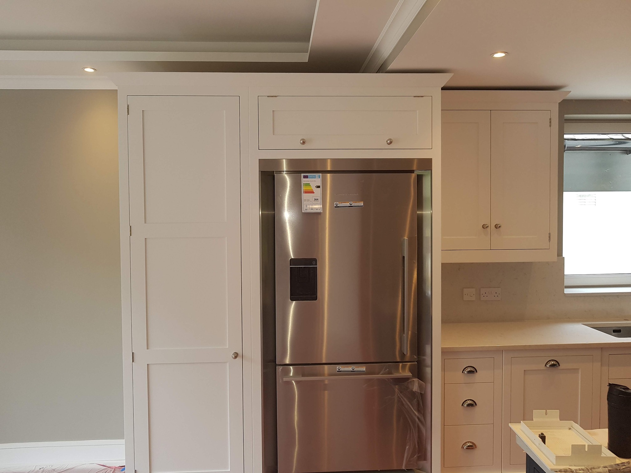 Kuchnia z zabudową meblową w odcieniach bieli, z wbudowaną lodówką ze stali nierdzewnej i oświetleniem punktowym w suficie.