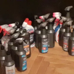 Zestaw różnych środków czyszczących w butelkach z rozpylaczami i bez, stojących na drewnianej podłodze w pomieszczeniu.