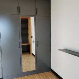 TSE Remonty - Szara szafa wnękowa z lustrzanym frontem, w której widać biurko z półkami i lampką, drewniana podłoga i listwy przypodłogowe.