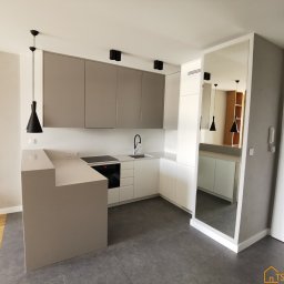 TSE Remonty - Nowoczesna, jasna kuchnia w Piasecznie z szarymi szafkami górnymi i białymi dolnymi, wykończona blatem w kolorze szarym, z czarnymi lampami wiszącymi i oświetleniem punktowym, odbita w lustrzanej...