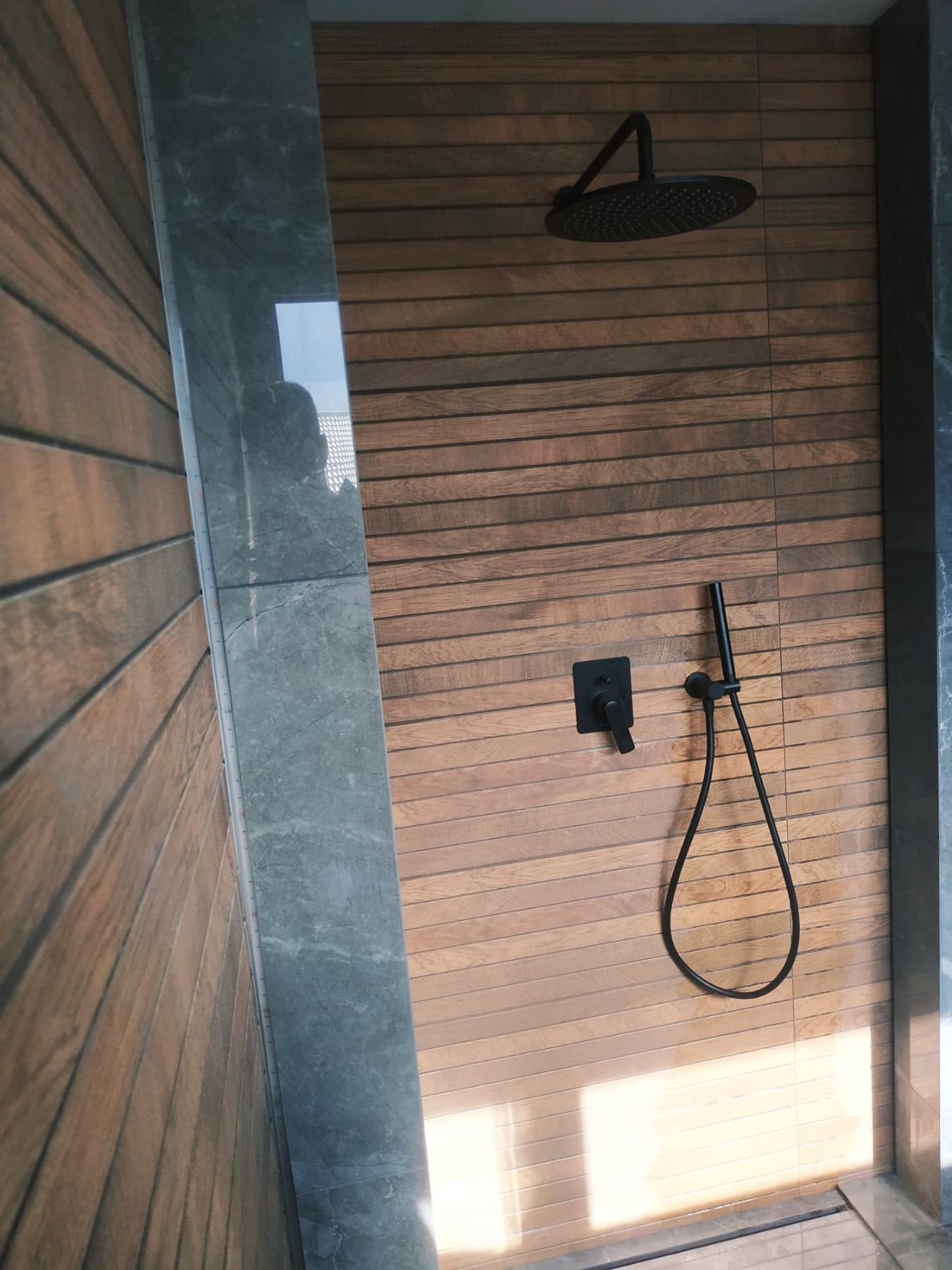 Nowoczesna kabina prysznicowa z drewnianymi panelami ściennymi i czarną armaturą, widok z dołu.