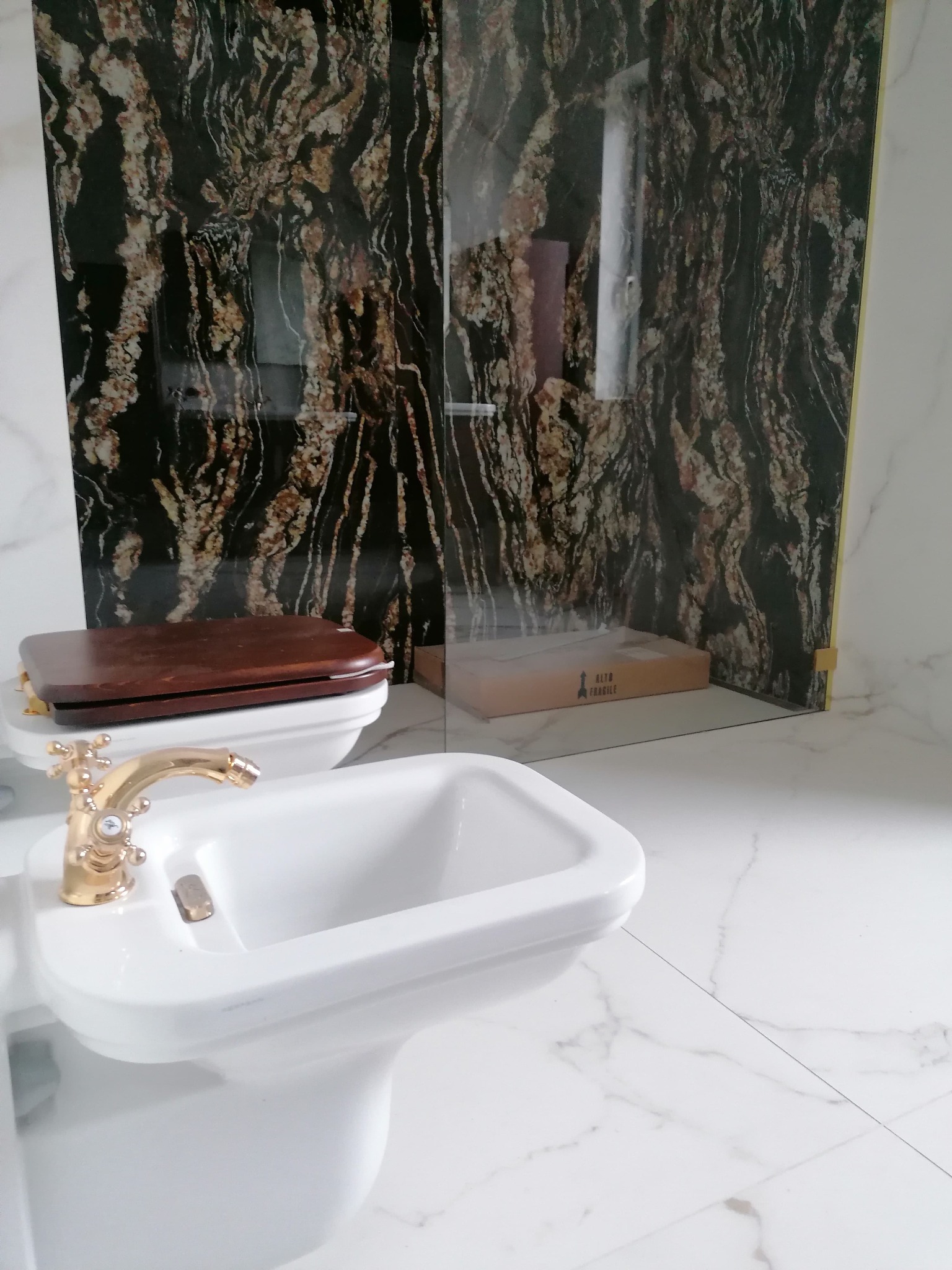 Nowoczesna łazienka z białymi marmurowymi płytkami, złotą armaturą bidetu i ścianą z czarnego marmuru z brązowymi żyłami.