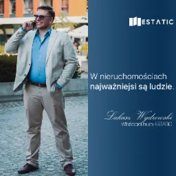 Mężczyzna w beżowym garniturze i okularach przeciwsłonecznych rozmawia przez telefon na tle budynku. Po prawej stronie logo firmy i hasło reklamowe związane z nieruchomościami.