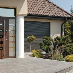 Zakład Stolarski ART-TOM - Nowoczesne wejście do domu z brązowymi skrzydłami z przeszkleniami, białą kolumną i szarą bramą garażową roletową.