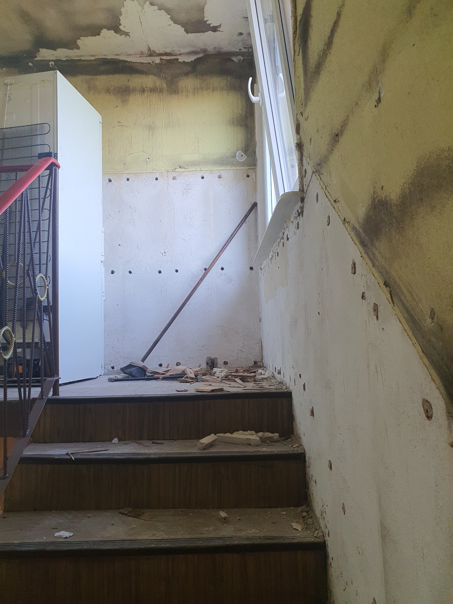 Schody w trakcie remontu w Szczecinie, widoczne ślady po usuniętych elementach na ścianie, surowy stan wykończenia z widocznymi uszkodzeniami i pozostałościami po pracach budowlanych.