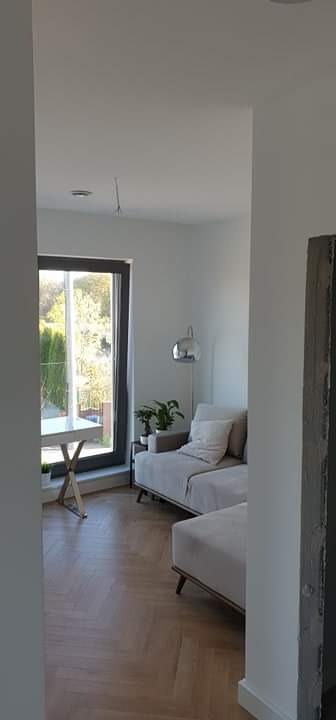 Jasne wnętrze po remoncie: świeżo pomalowane ściany, parkiet ułożony w jodełkę, nowoczesna sofa i lampa.