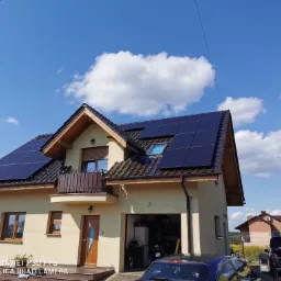 Dom jednorodzinny z zamontowanymi panelami fotowoltaicznymi na dachu, widoczne błękitne niebo z białymi chmurami.