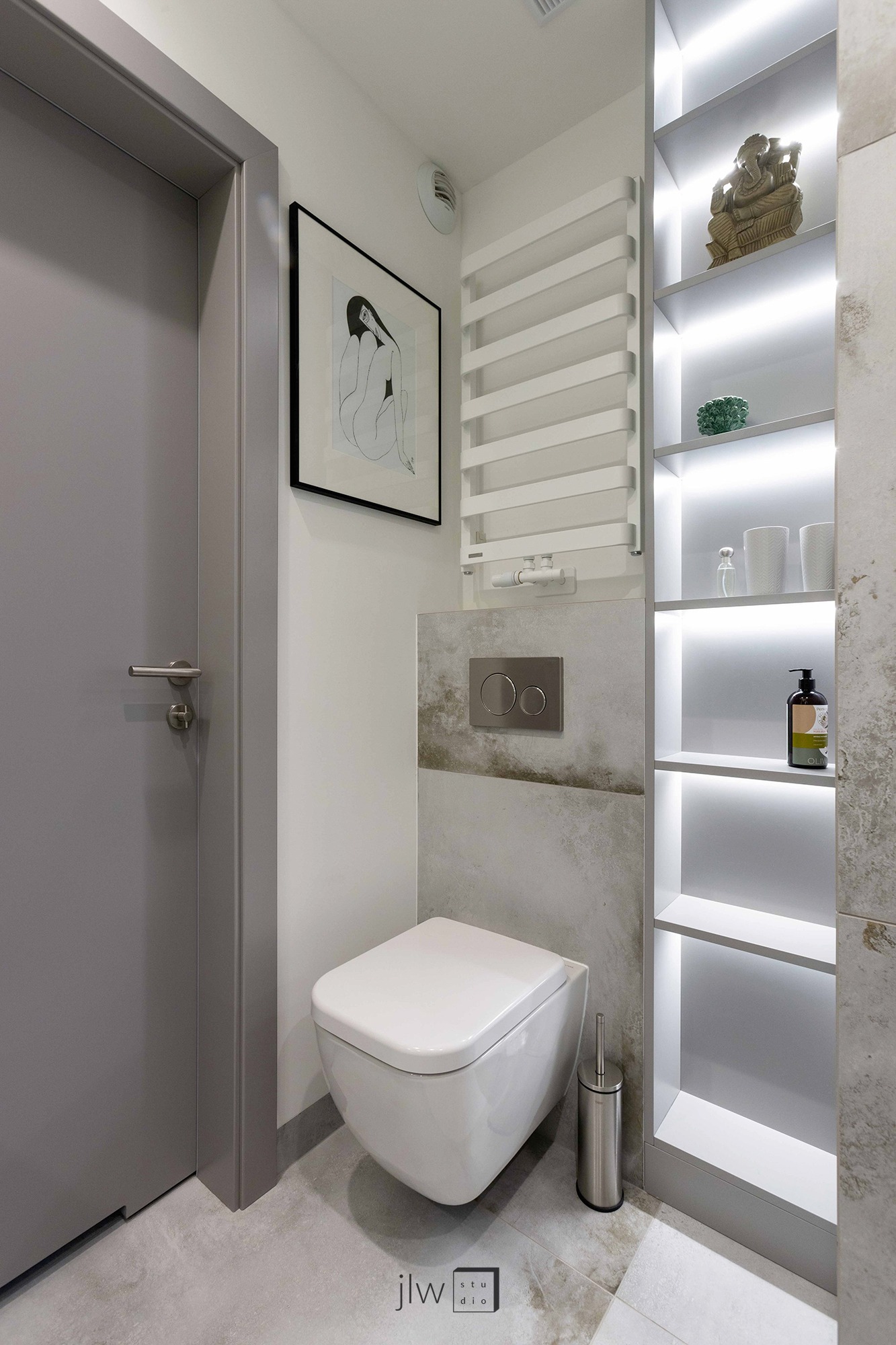 Nowoczesna toaleta podwieszana z szarą ramą, ceramiczną okładziną i podświetlanymi półkami z dekoracjami, w tym figurką Buddy, oraz obrazkiem w czarnej ramie.