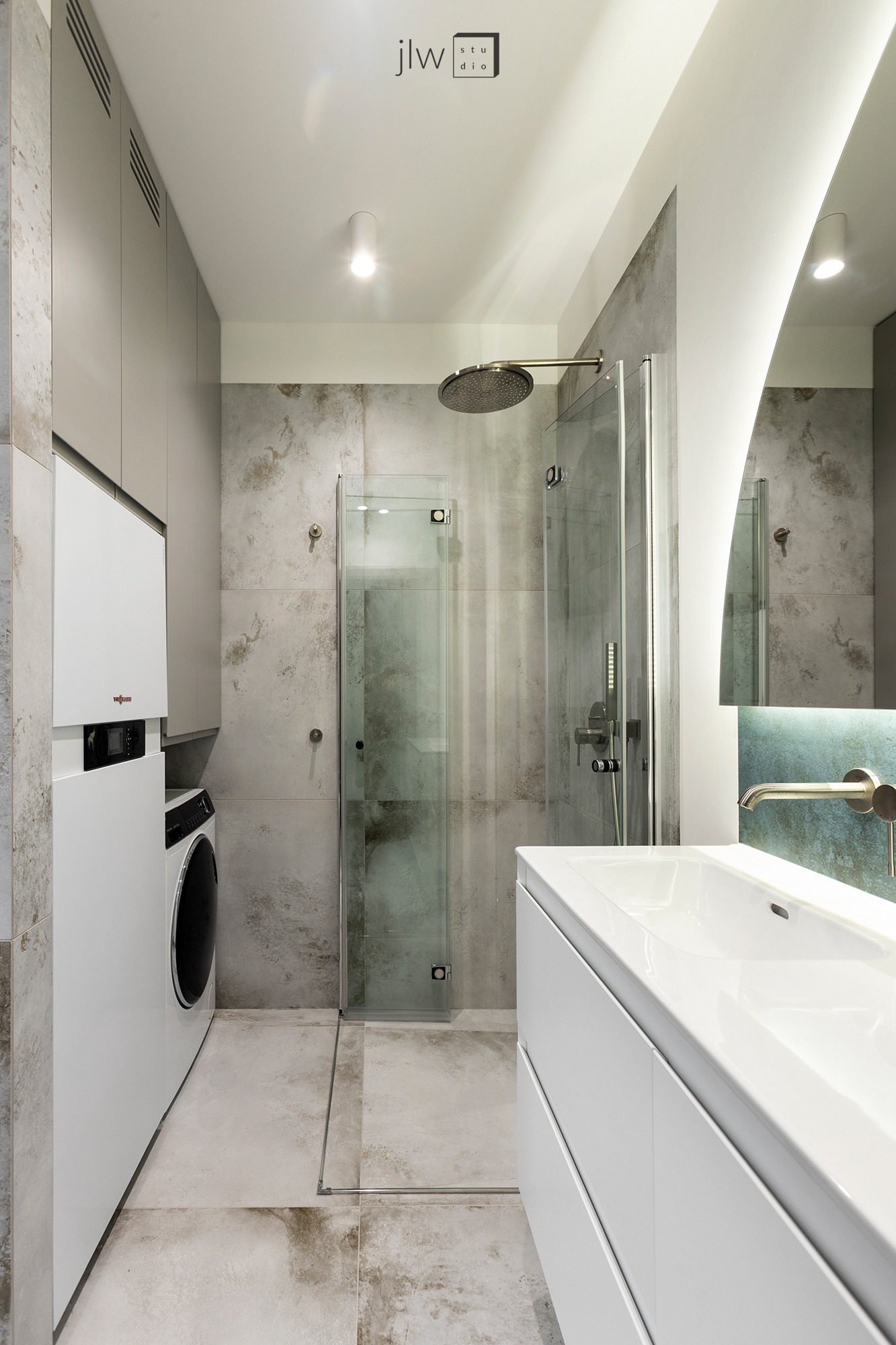 Nowoczesna łazienka w Warszawie z kabiną prysznicową typu walk-in, pralką ukrytą w zabudowie meblowej oraz umywalką z szafką, utrzymana w szaro-białej kolorystyce z akcentami mosiądzu.