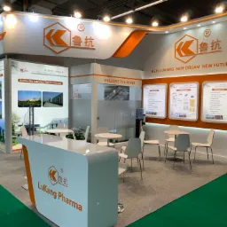 Stoisko targowe firmy LuKang Pharma na targach CPHI 2019 we Frankfurcie, z logo firmy w pomarańczowym kolorze, białymi meblami i informacjami o produktach na ścianach.