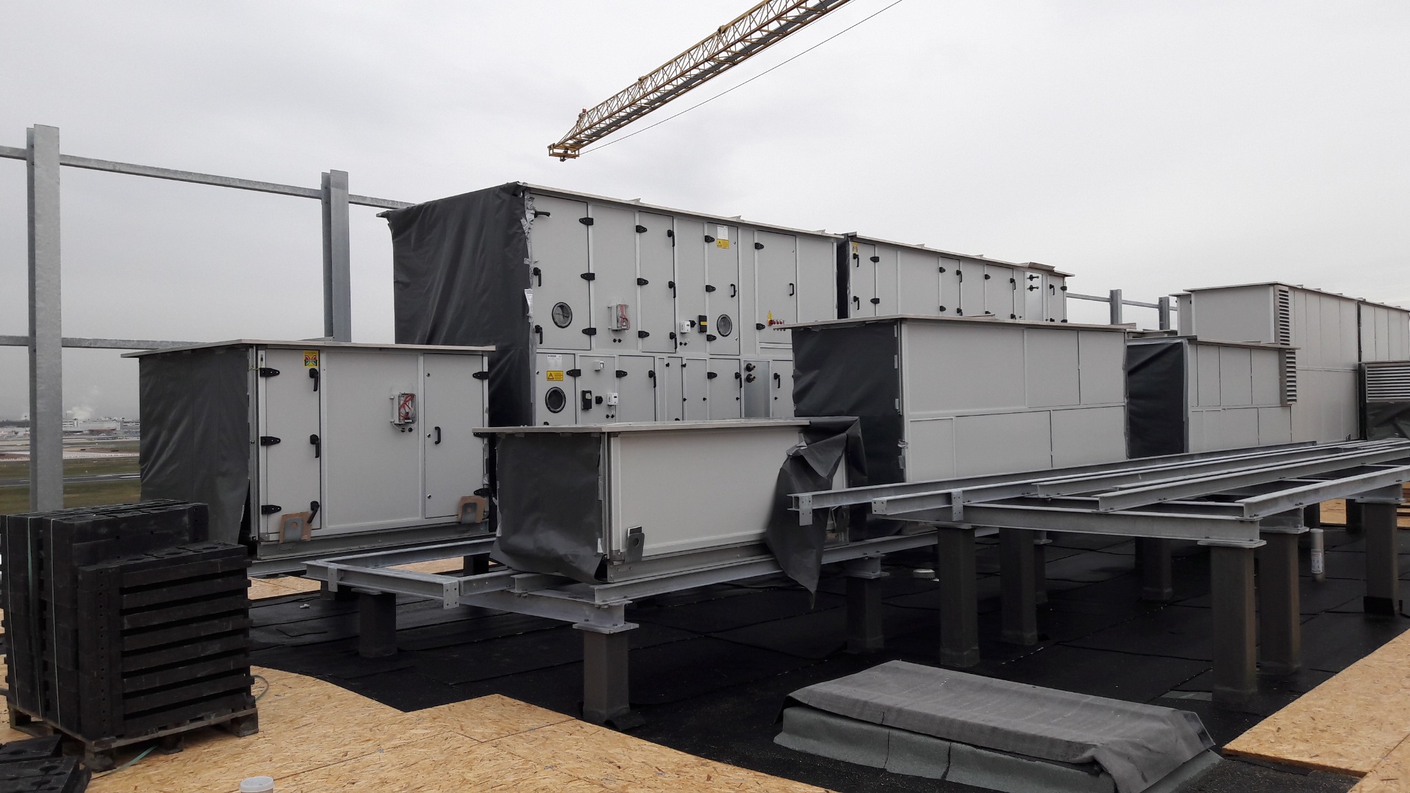 Instalacja przemysłowa na dachu budynku z widocznym dźwigiem w tle, prawdopodobnie system wentylacyjny lub klimatyzacyjny.