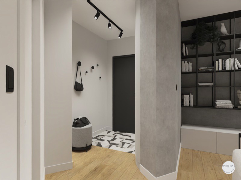Nowoczesny przedpokój z drewnianą podłogą, czarną listwą oświetleniową, wieszakami na ścianie, pufą i geometryczną posadzką przy drzwiach wejściowych, widoczny regał z książkami w tle.