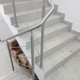 Schody z szarego kamienia z zamontowaną balustradą ze stali nierdzewnej, z widocznymi pudełkami po produktach budowlanych u podstawy balustrady.