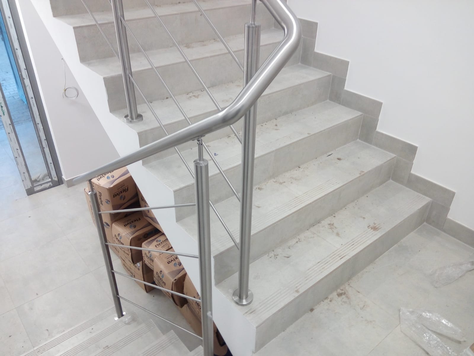 Schody z szarego kamienia z zamontowaną balustradą ze stali nierdzewnej, z widocznymi pudełkami po produktach budowlanych u podstawy balustrady.