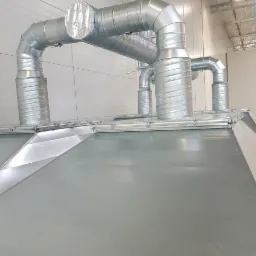 System kanałów wentylacyjnych z blachy ocynkowanej, widok z dołu na elementy łączeniowe i izolację na jednym z odcinków, w tle hala przemysłowa.