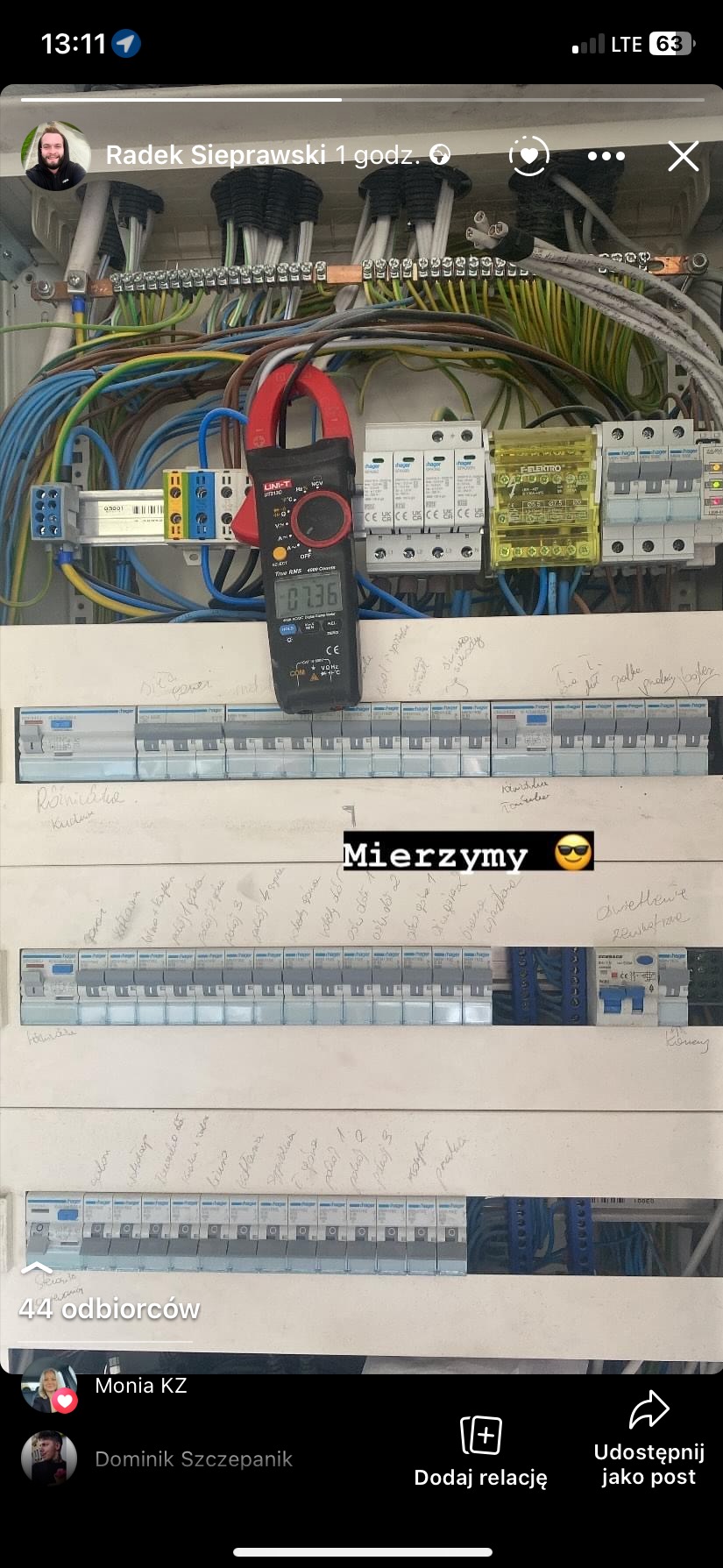 Pomiar napięcia w rozdzielnicy elektrycznej za pomocą miernika cęgowego UNI-T UT210C, widoczne zabezpieczenia Hager i opisane obwody.