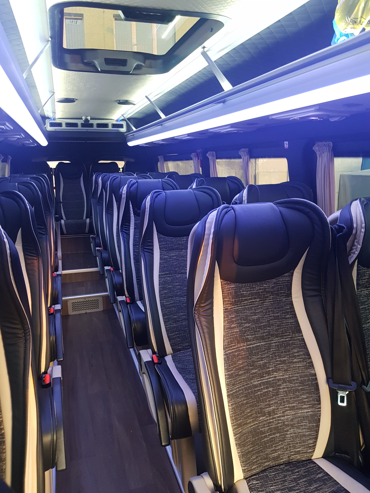 Wnętrze luksusowego busa z rzędami czarno-białych foteli z zagłówkami, oświetleniem LED i drewnianą podłogą.