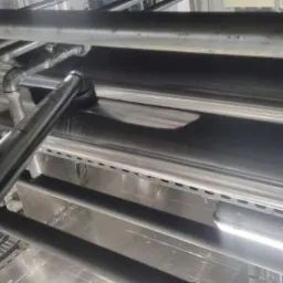 Metalowe rury i elementy konstrukcyjne pod sufitem hali przemysłowej, widoczne ślady kurzu i zabrudzeń na powierzchniach.