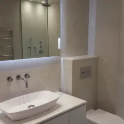 Nowoczesna łazienka z podświetlanym lustrem, wiszącą toaletą i umywalką nablatową w London, wykończona w jasnych, beżowych odcieniach.