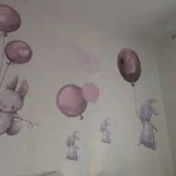 Ręcznie malowane, pastelowe króliki z balonami zdobią ścianę pokoju dziecięcego w Toruniu, tworząc bajkowy klimat.