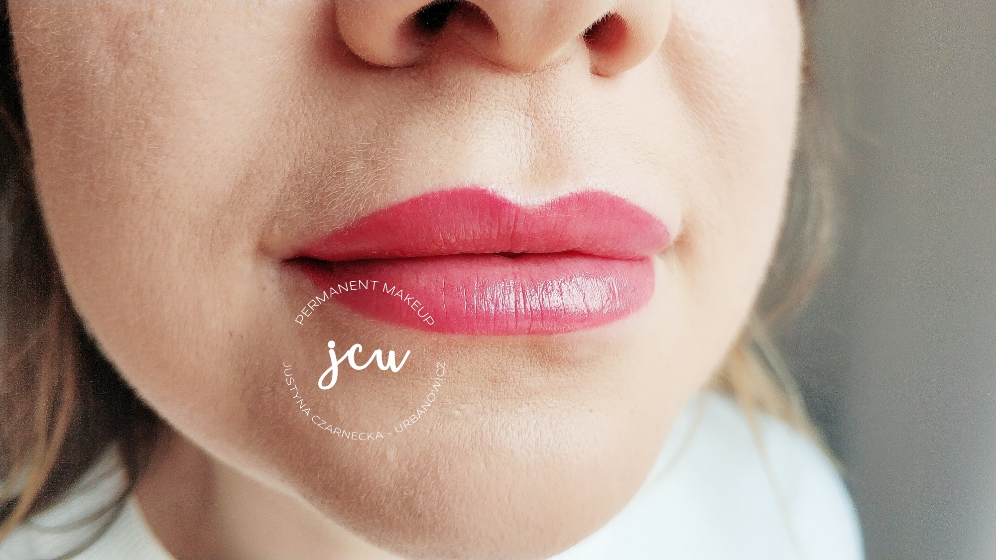 Zbliżenie na usta kobiety po zabiegu pigmentacji, z widocznym delikatnym różowym kolorem i błyszczącym wykończeniem, logo firmy widoczne na skórze.