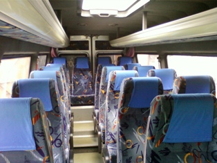 Wnętrze busa z rzędami niebieskich foteli z wzorzystą tapicerką, widok z przodu pojazdu, oświetlenie górne wzdłuż sufitu.