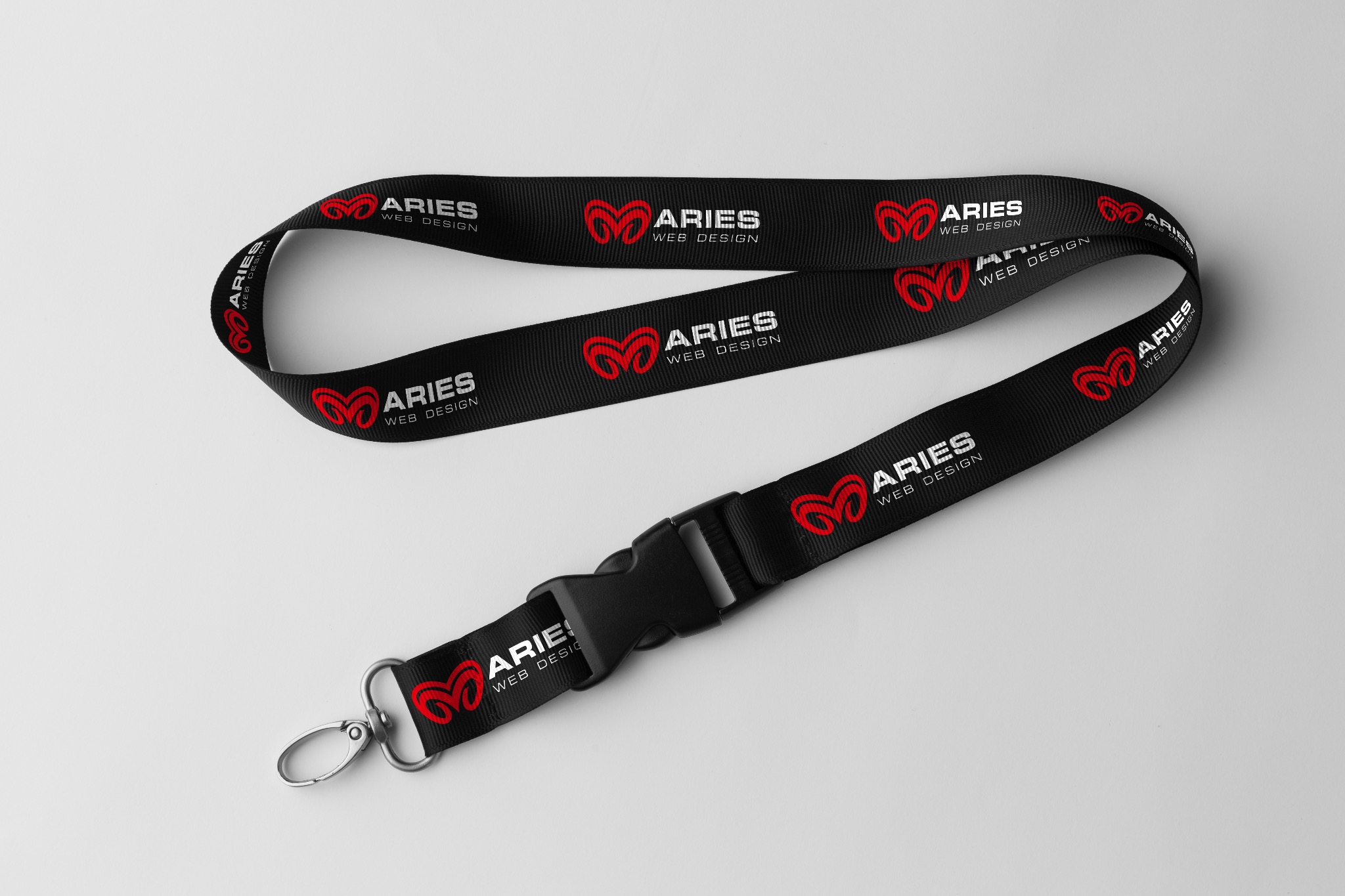 Czarna smycz z powtarzającym się logo i nazwą firmy 'Aries Web Design' w kolorze białym i czerwonym, leżąca na jasnoszarym tle.
