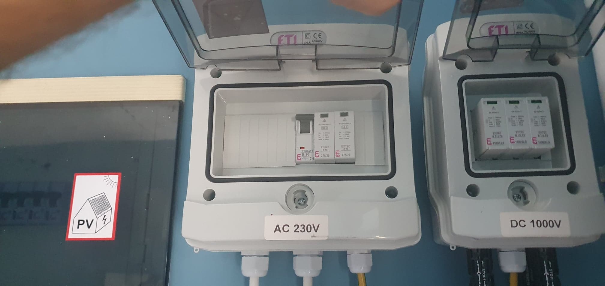 Rozdzielnica AC 230V i DC 1000V z zabezpieczeniami przepięciowymi ETI w białych obudowach, z naklejką PV na boku, zamontowane na niebieskiej ścianie.