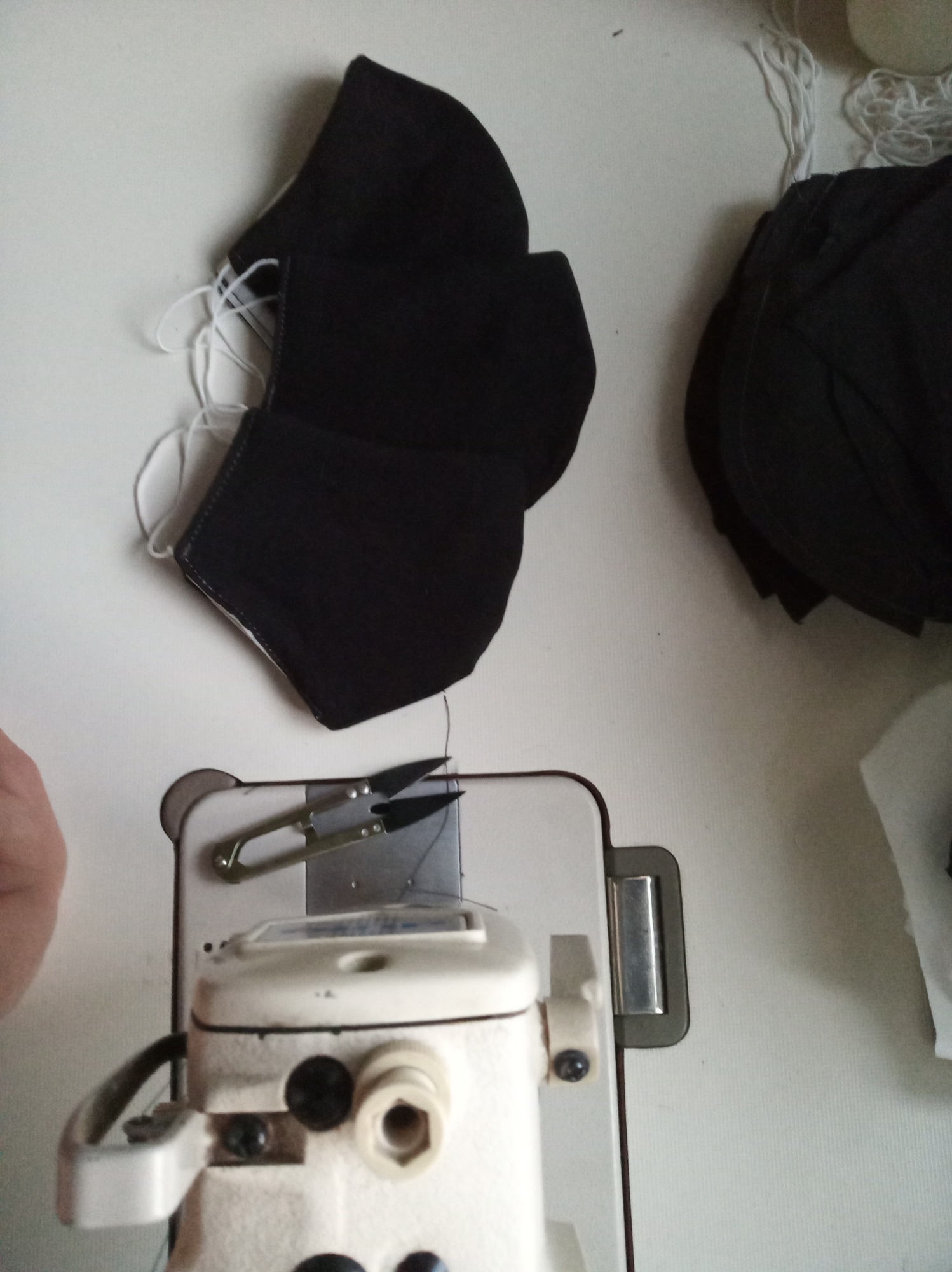 Proces produkcyjny: Czarna, bawełniana maska ochronna leży obok maszyny do szycia, na której znajdują się małe nożyczki do obcinania nici.