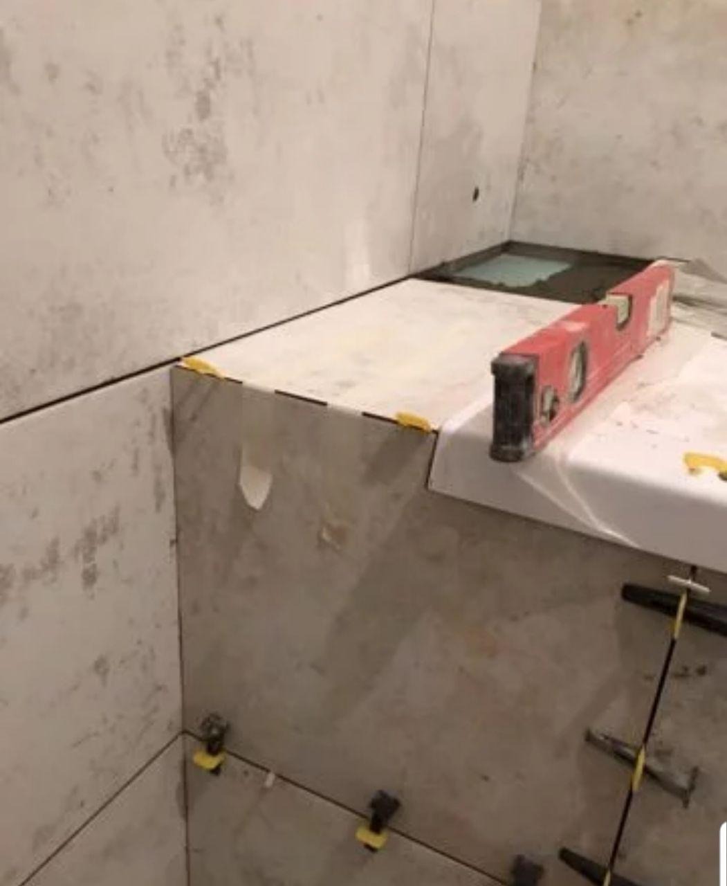 Układanie płytek w łazience: poziomica spoczywa na świeżo położonych płytkach, widoczne krzyżyki dystansowe i system poziomowania płytek.