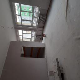 Łukaszbud - Przygotowane do prac wykończeniowych wnętrze mieszkania z zabezpieczoną podłogą, widoczne okna i fragment ściany z otwartym przejściem.