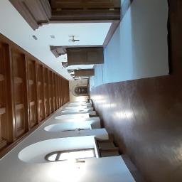 Łukaszbud - Długi korytarz z drewnianą boazerią, białymi ścianami z łukami i oknami, oraz polerowaną podłogą, perspektywa z jednego końca.