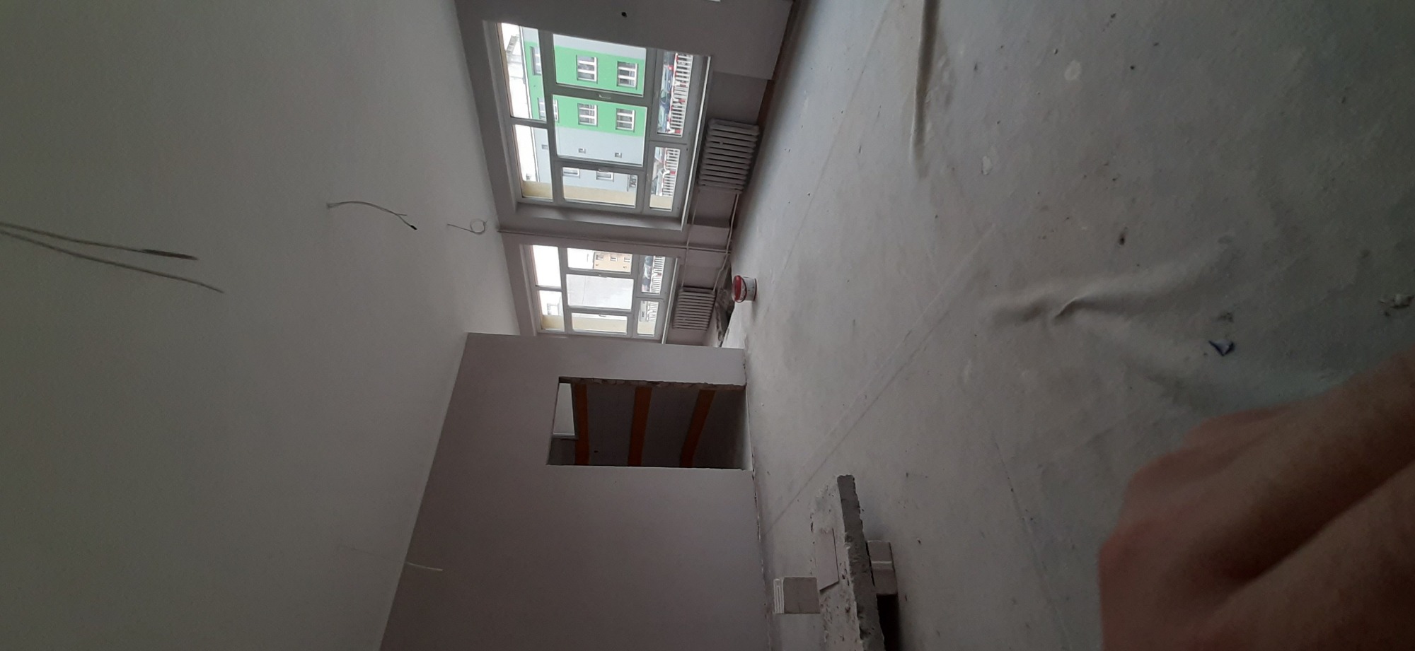 Przygotowane do prac wykończeniowych wnętrze mieszkania z zabezpieczoną podłogą, widoczne okna i fragment ściany z otwartym przejściem.