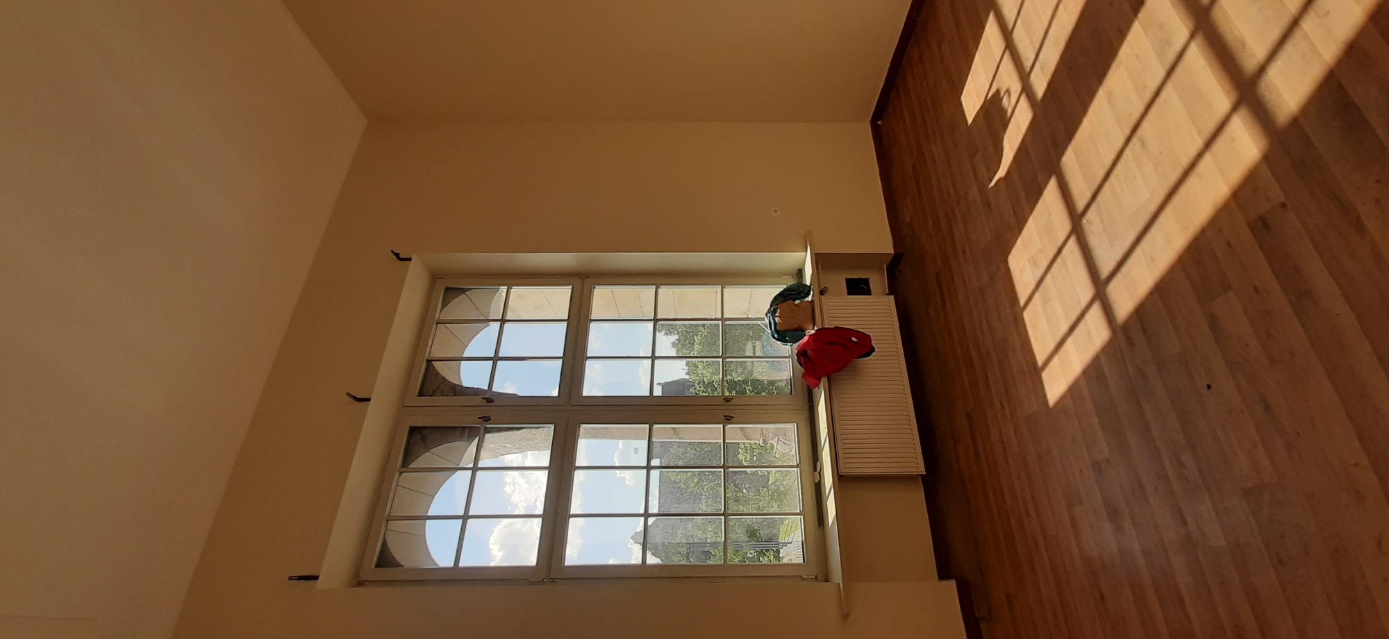 Jasne wnętrze z drewnianą podłogą, dużym oknem z widokiem na zewnątrz, na kaloryferze suszą się ubrania