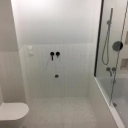 Wykończona łazienka w stylu minimalistycznym z białymi, wąskimi płytkami ułożonymi pionowo, czarną armaturą i kabiną prysznicową z czarnymi ramami.