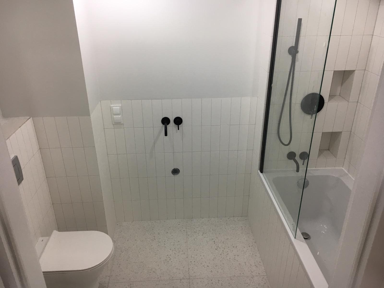 Wykończona łazienka w stylu minimalistycznym z białymi, wąskimi płytkami ułożonymi pionowo, czarną armaturą i kabiną prysznicową z czarnymi ramami.