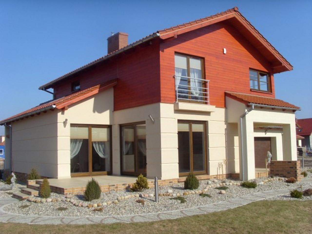 Dwukondygnacyjny dom jednorodzinny z drewnianą elewacją na górnej kondygnacji, jasną elewacją na dole, małym balkonem i brukowanym obejściem