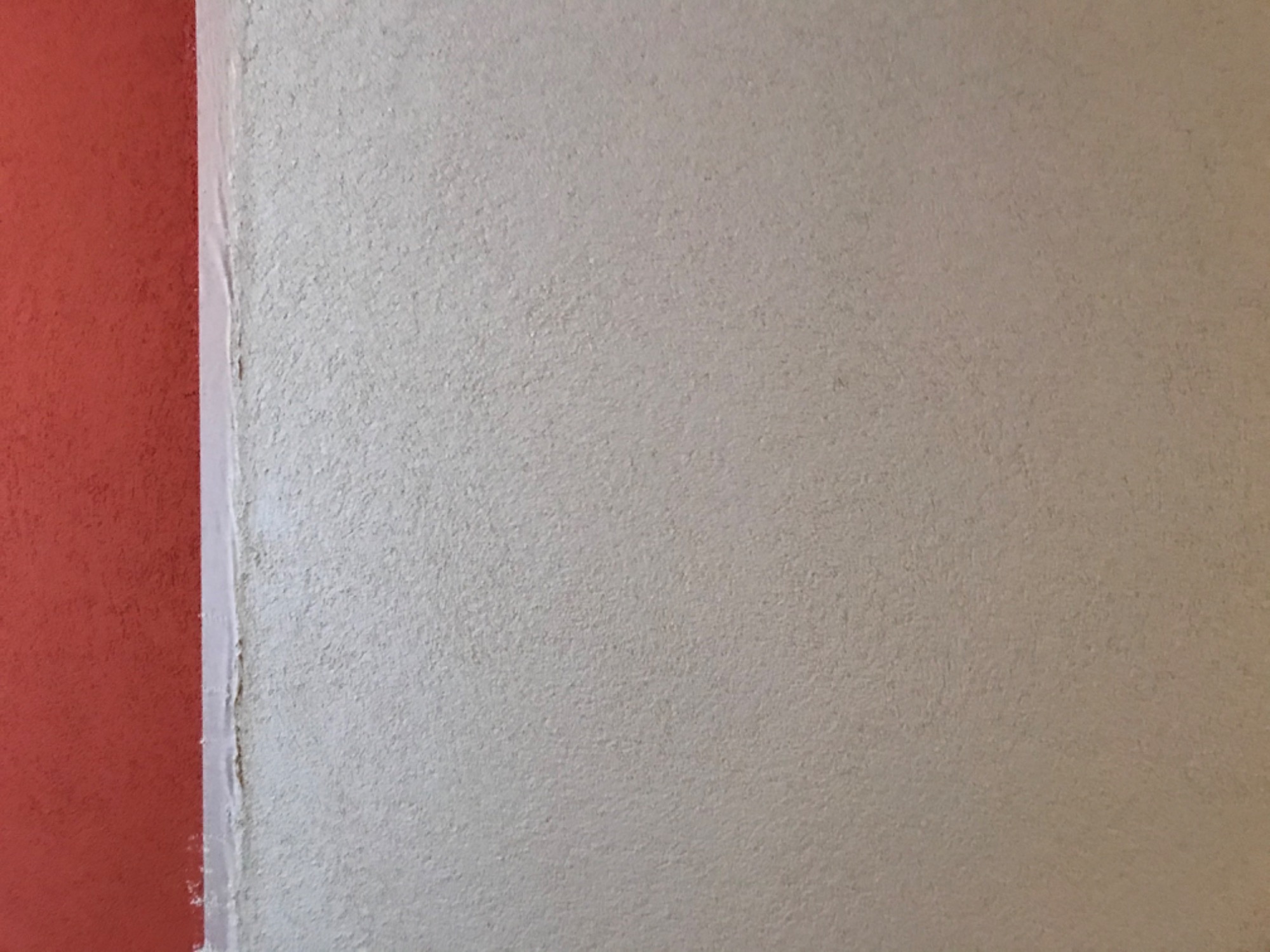 Fragment ściany z fakturą strukturalną w odcieniach beżu, sąsiadujący z pionowym pasem ściany pomalowanej na czerwono, oddzielone białą listwą.