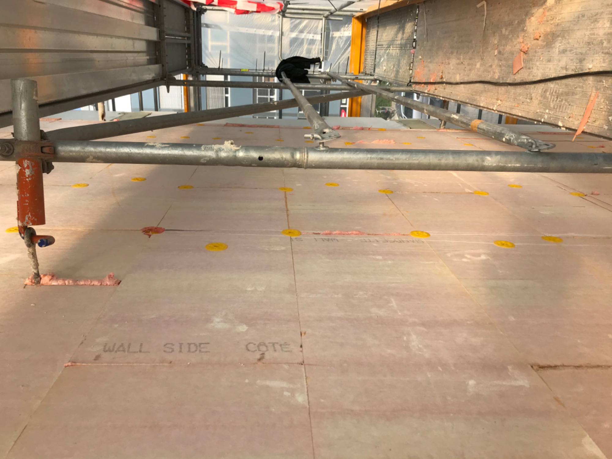 Widok z góry na rusztowanie i płyty izolacyjne z napisem 'WALL SIDE COTE', zamontowane na elewacji budynku w trakcie prac budowlanych.