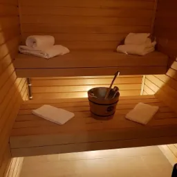 Wnętrze sauny z drewnianymi ławkami, ręcznikami i drewnianym wiadrem z chochlą.