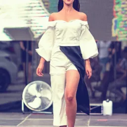 Modelka prezentuje asymetryczny, biało-czarny komplet odzieży na wybiegu, z wentylatorem w tle.