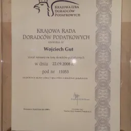 Skan dyplomu Krajowej Rady Doradców Podatkowych potwierdzającego wpis Wojciecha Gut na listę doradców podatkowych w dniu 22.09.2008, oprawiony w ramkę z pleksi, widoczne śruby mocujące.