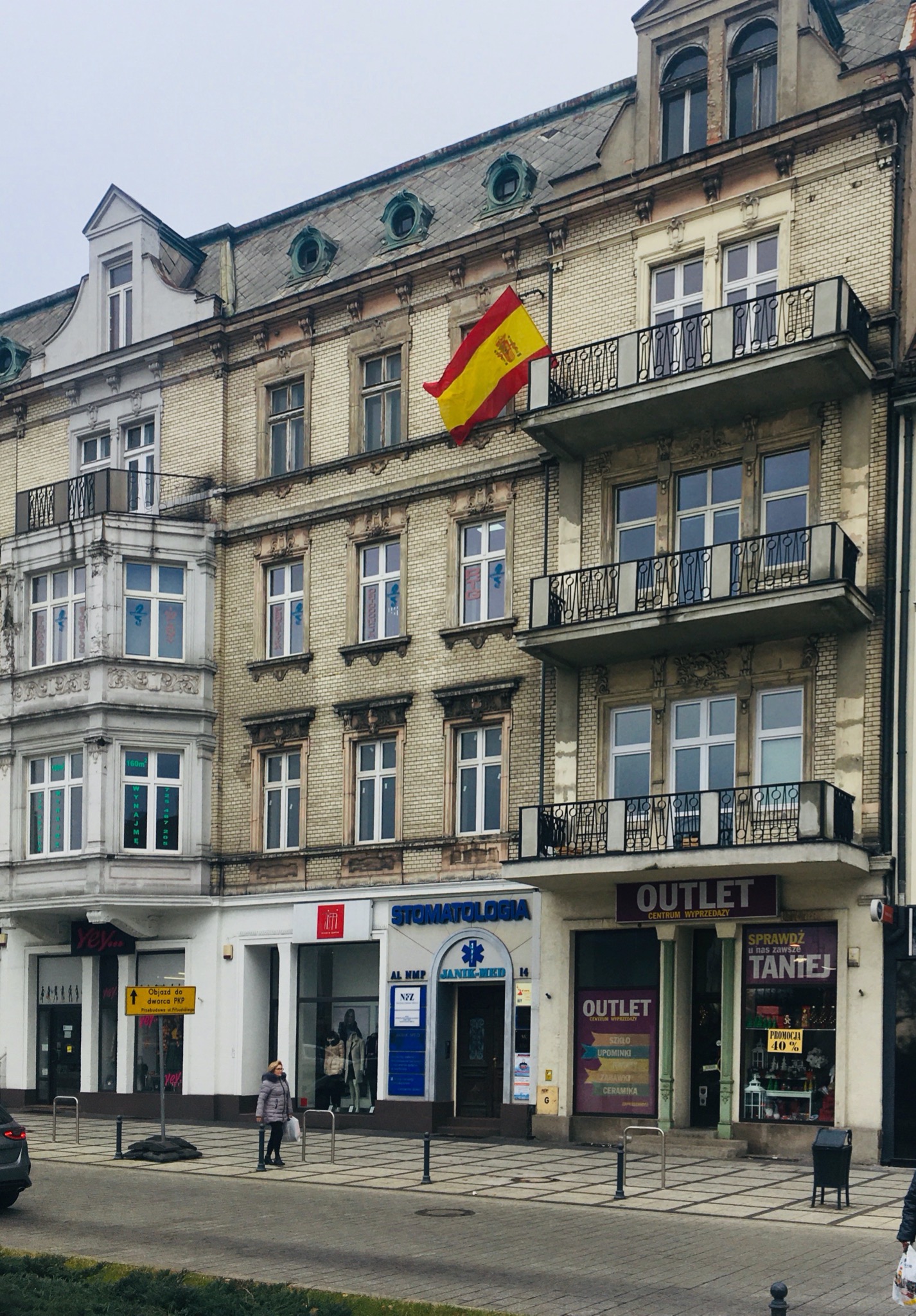 Budynek szkoły językowej z hiszpańską flagą na balkonie, widok z ulicy w pochmurny dzień.